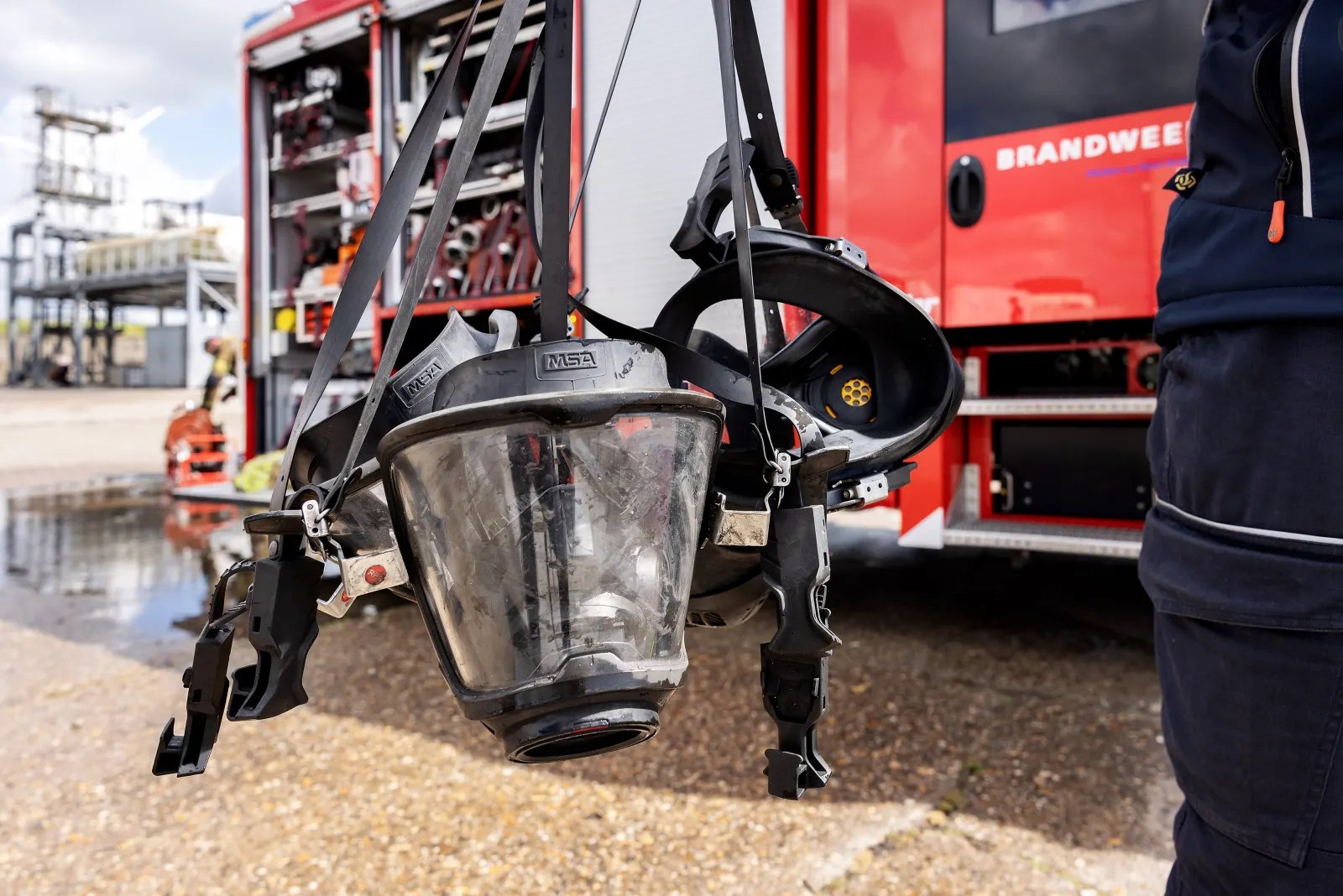 Ademluchtmasker in de hand, met een brandweerauto op de achtergrond